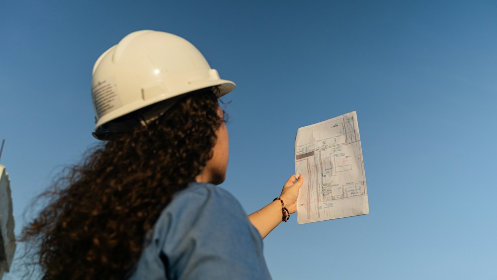A woman in a hard hat checking a drawing against the site