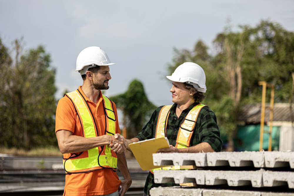 Two supervisors in hard hats shaking hands on site