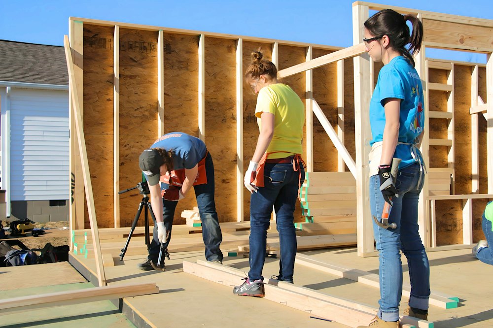 A framing crew, women and men, putting up a wall on a house