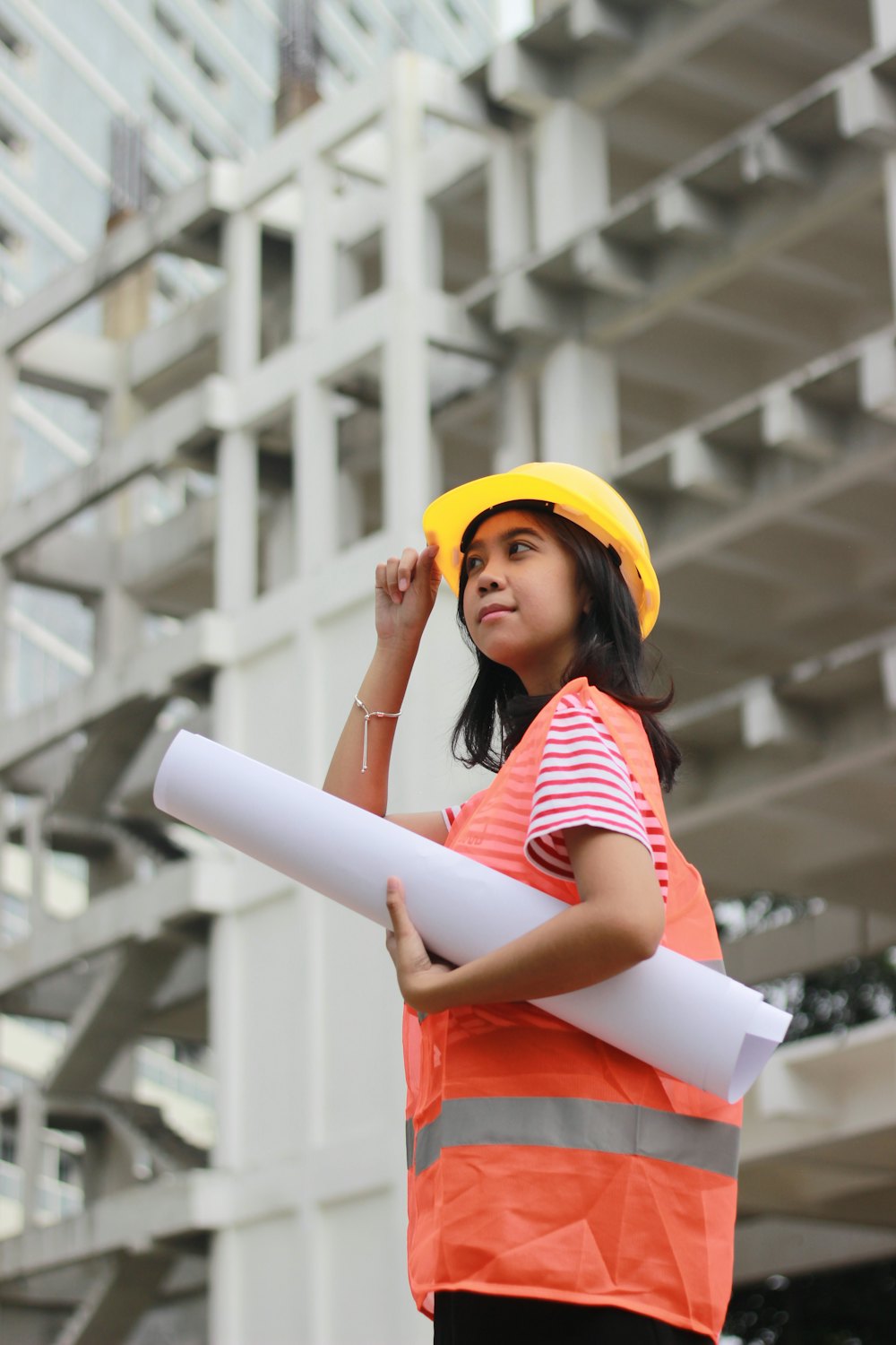 A young woman in a yellow hard hat holding rolled drawings