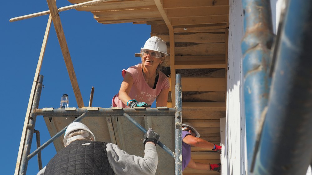 A woman in a hard hat working from a scaffold on a house frame