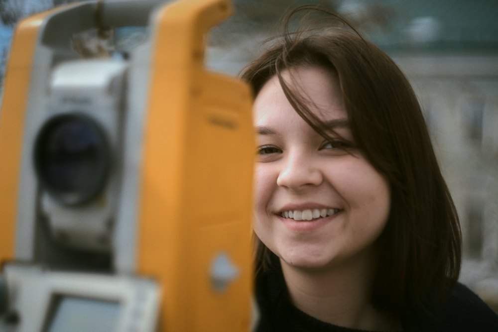 A smiling woman beside a surveying instrument