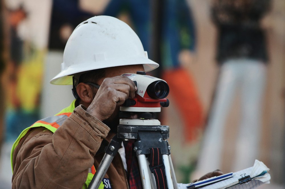 A surveyor in a hard hat sighting through a level